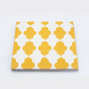 May include: A yellow and white ceramic tile with a geometric pattern. The tile has a white background with a repeating pattern of yellow quatrefoils.