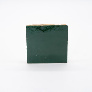 May include: A square tile with a dark green glaze and a rough, uneven edge.