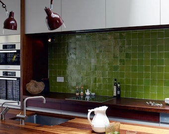 May include: A kitchen island with a wooden countertop and a stainless steel sink. The island has drawers and a white pitcher with green glasses on the countertop. The kitchen has green tile backsplash and a stainless steel oven.