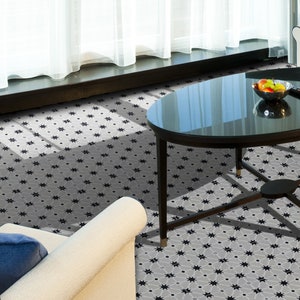 May include: A black and white geometric tile floor with a star pattern. A black oval table with a glass top sits on the floor. A white chair with a blue cushion is in the foreground.