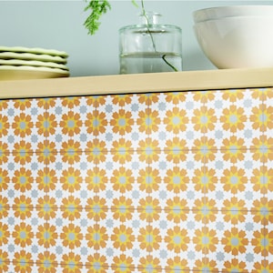 May include: A close-up of a tiled wall with a geometric pattern. The tiles are a light yellow color with a white and gray starburst design.