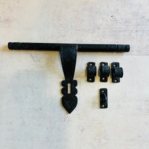 May include: A black, ornate door latch set. The set includes a long, horizontal bar, a decorative keyhole plate, three loop-shaped brackets, and a small rectangular handle. The metal has a textured finish and decorative patterns.