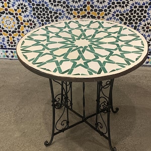 May include: Round outdoor table with a mosaic tile top featuring a green star pattern on a white background. The table has a dark metal frame with decorative scrollwork and measures approximately 30 inches in diameter.
