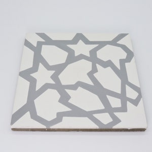 May include: A white ceramic tile with a gray geometric pattern. The pattern features stars and abstract shapes.
