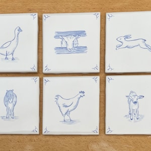 May include: A set of six square white ceramic tiles, each featuring a blue hand-painted illustration of a farm animal. The designs include a goose, a sheep behind a fence, a running rabbit, a horse, a chicken, and a calf, all with corner accents.