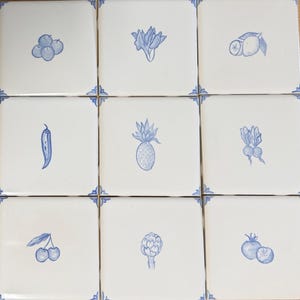 May include: Nine white square tiles with blue hand-drawn illustrations of fruits and vegetables, including blueberries, a flower, a lemon, a chili pepper, a pineapple, beets, cherries, an artichoke, and tomatoes. Each tile has blue corner accents.