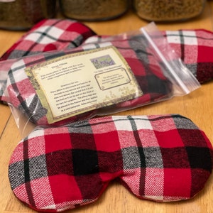 Könnte beinhalten: Roter und schwarzer karierter Augen-Maske mit einem weißen Etikett, auf dem "Stress Pillow" steht. Das Etikett enthält Gebrauchsanweisungen und listet die Zutaten auf: Lavendel, Kamille und Rosmarin.