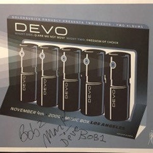 以下が含まれることがあります： バンドDevoのフレーム入りプリント。プリントは、バンド名と「Two Nights, Two Albums」のテキストが入った暗い背景です。5つの黒と銀の円筒形のオブジェクトが表示されています。プリントには2005年11月4日の日付が含まれています。