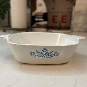 May include: A white, rectangular casserole dish with a blue floral design. The dish has two handles and is made of ceramic. A classic piece of kitchenware.