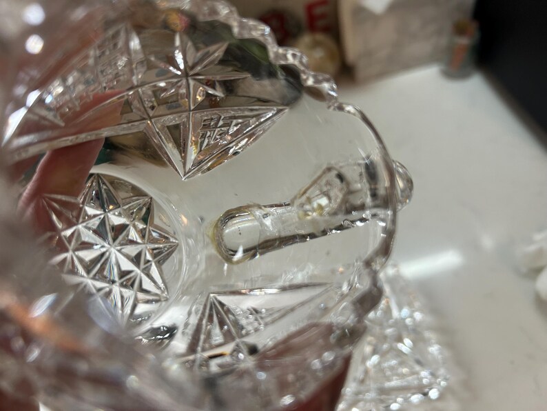 May include: Clear crystal glass with starburst and geometric patterns. The glass has a cut design with a textured surface. The image shows a close-up of the glass, highlighting the intricate details and clarity of the material.