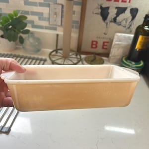 May include: A rectangular, light-orange baking dish with rounded corners and a slightly raised rim. The dish is held by a hand, showcasing its shape and color. It appears to be made of glass or a similar material.