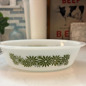 May include: White oval serving dish with a green floral pattern around the bottom. The dish has a slightly raised rim and is made of a durable, heat-resistant material. A classic piece for serving food.