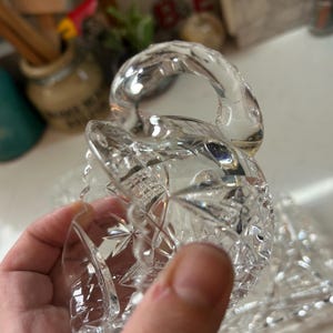 May include: A clear, cut-glass serving dish with a handle. The dish features a starburst and diamond pattern. The handle is curved and smooth. The dish is held in a hand.