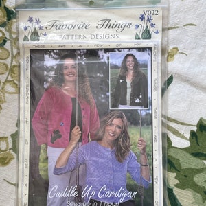 May include: A pattern design for a "Cuddle Up Cardigan" sewing project. The pattern includes instructions for a cardigan that can be sewn in one hour. The image shows two women wearing the cardigan in different colors.