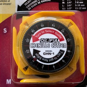 May include: A yellow and black chenille cutter with a dial to select the cutting width. The dial has markings for 1/4 inch, 3/8 inch, and 1/2 inch. The cutter is labeled "OLFA Chenille Cutter" and "Model CHN-1".