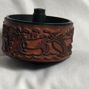 May include: A brown rubber stamp with a detailed design of palm trees and waves. The stamp is mounted on a black plastic base with a metal spindle.