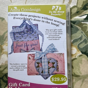 May include: A clear plastic case containing a product by Anita Goodesign. The case features a pink and blue gift card holder design with the text "Just for you!" and "Gift Card Holders". The text "Create these projects without sewing! Everything's done in the hoop!" is also visible.