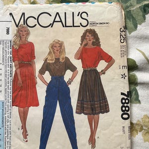 May include: A sewing pattern for a top, skirt, and pants. The pattern is for a size 14, bust 36. The pattern is from McCall's and is designed by Liz Claiborne. The pattern shows a red top with short sleeves, a brown and white striped skirt, and blue pants.