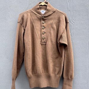 May include: A brown sweater with a high collar and a button-down placket. The long-sleeved sweater is made of a soft material and has ribbed cuffs and a ribbed hem. The sweater is hanging on a wooden hanger.