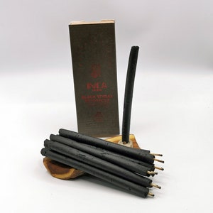 May include: A box of black styrax incense sticks with the brand name "INCA" and the text "BLACK STYRAX RESINA LIQUIDA" printed on the box. The sticks are arranged on a wooden stand.