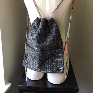 May include: Black and white drawstring backpack with a small pocket on the front. The straps are made of a colorful fabric with red, white, and blue accents.