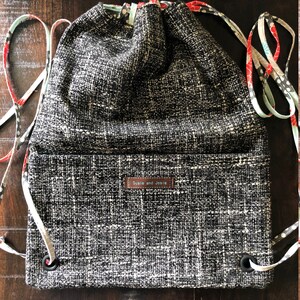 May include: Black and white drawstring bag with a black and white patterned fabric. The bag has a brown leather label that says "Susie and Josie".