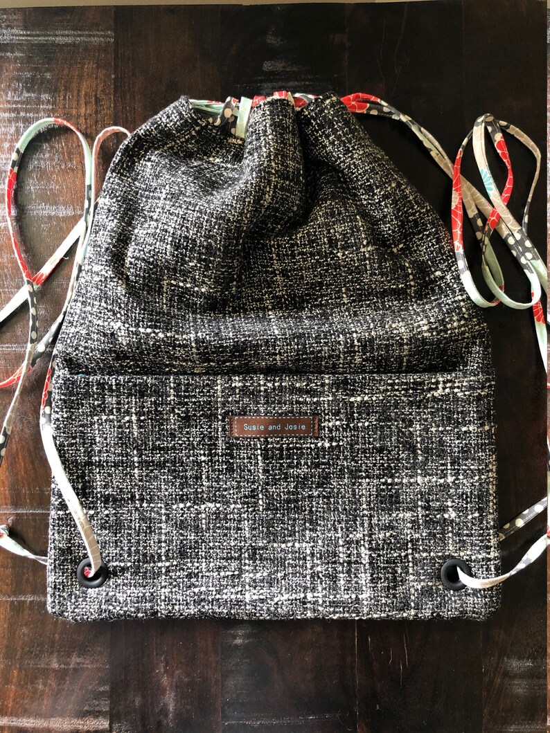 May include: Black and white drawstring bag with a black and white patterned fabric. The bag has a brown leather label that says "Susie and Josie".