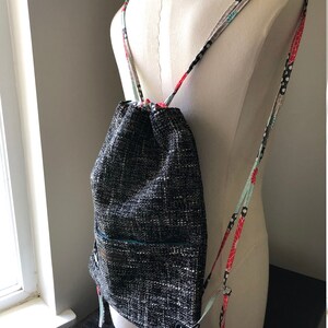May include: A black and white drawstring backpack with a small pocket on the front. The straps are made of colorful fabric with floral and polka dot patterns.