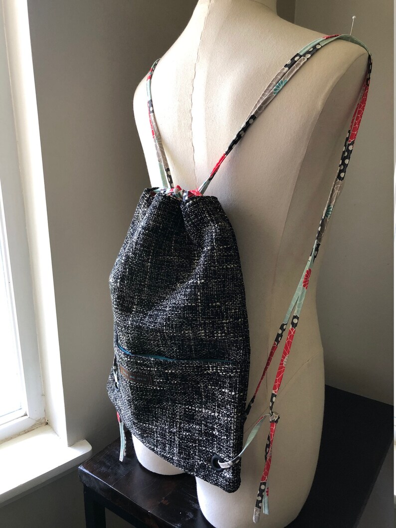 May include: A black and white drawstring backpack with a small pocket on the front. The straps are made of colorful fabric with floral and polka dot patterns.