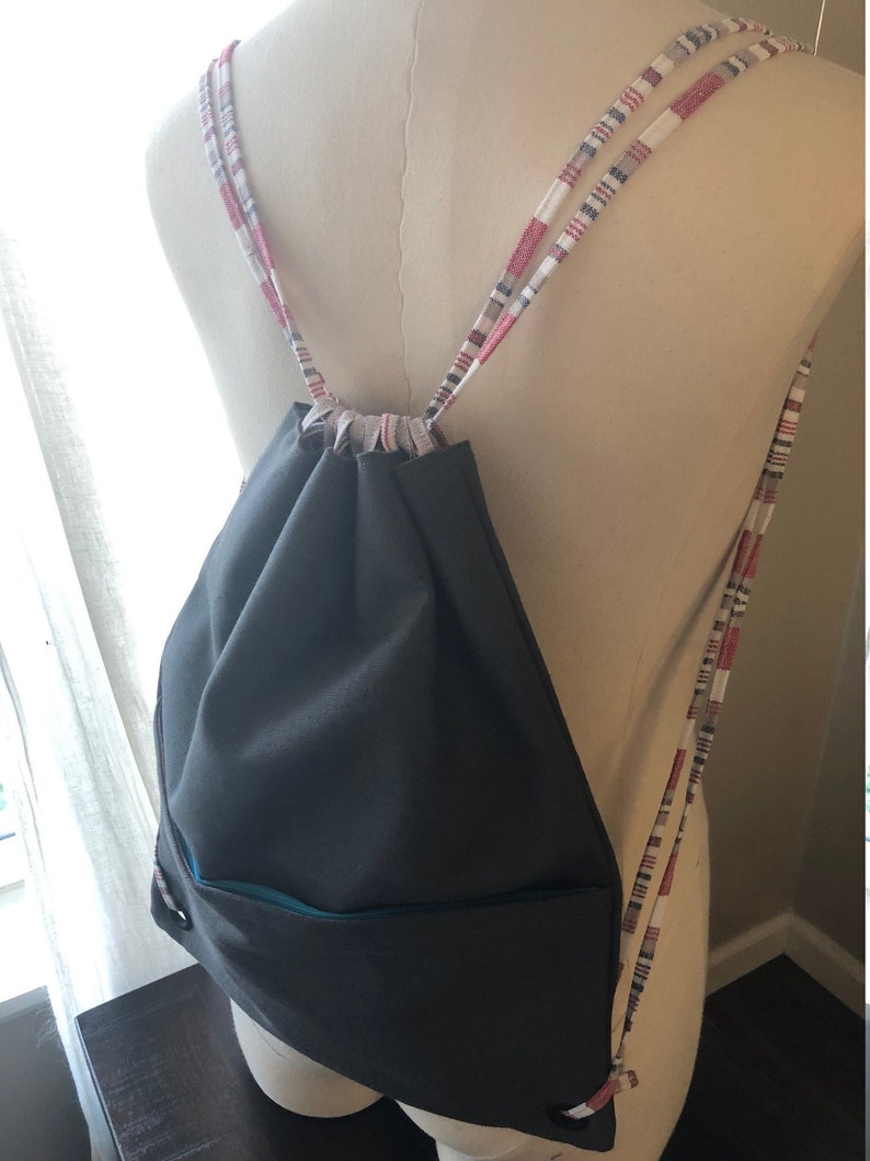 May include: A gray drawstring bag with a teal trim and red, white, and gray striped drawstrings.