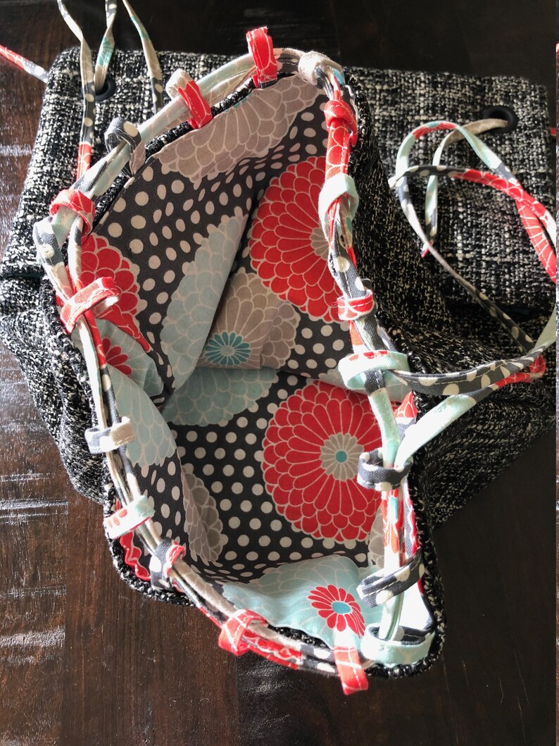 May include: A black and white fabric tote bag with a floral lining. The lining features red, blue, and white flowers on a black background with white polka dots.