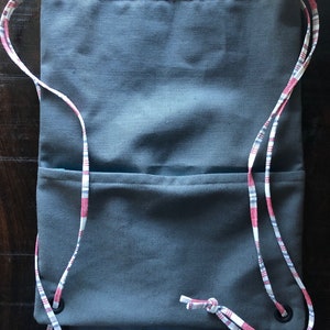 May include: A gray drawstring bag with a red and white plaid trim. The bag has two compartments and a drawstring closure.