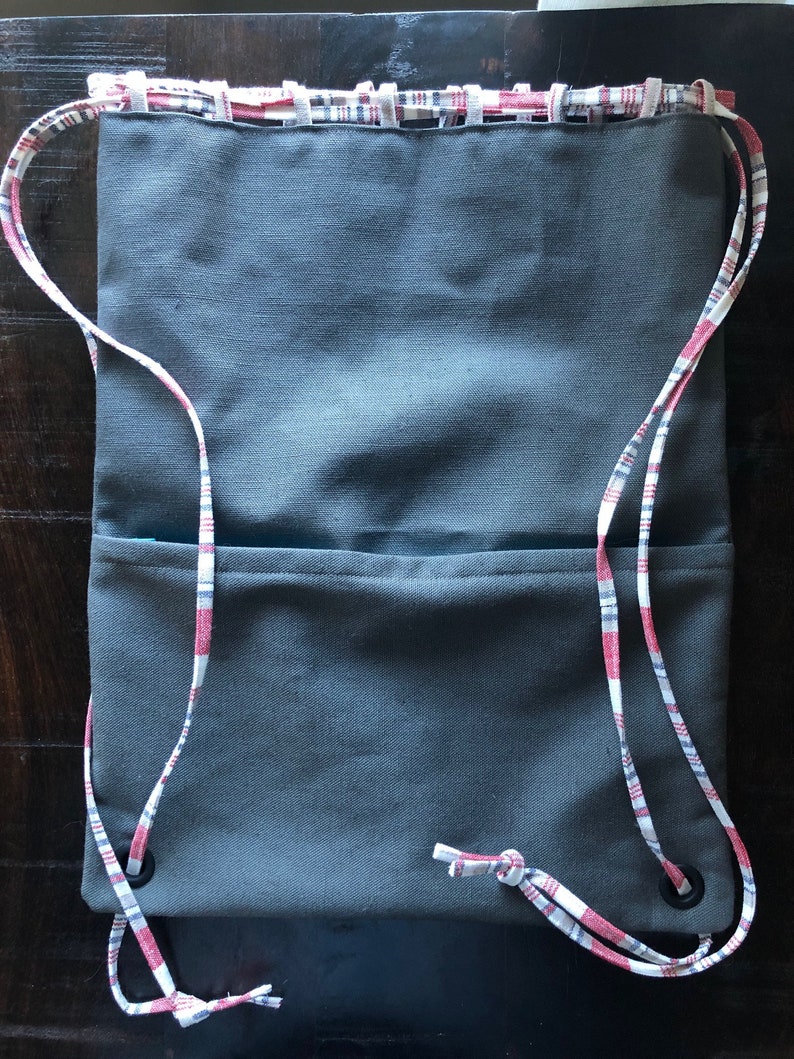 May include: A gray drawstring bag with a red and white plaid trim. The bag has two compartments and a drawstring closure.