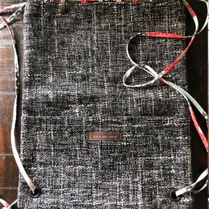 May include: A black and white woven drawstring bag with a brown leather tag that says "Susie and Josie". The bag has a floral patterned fabric trim.