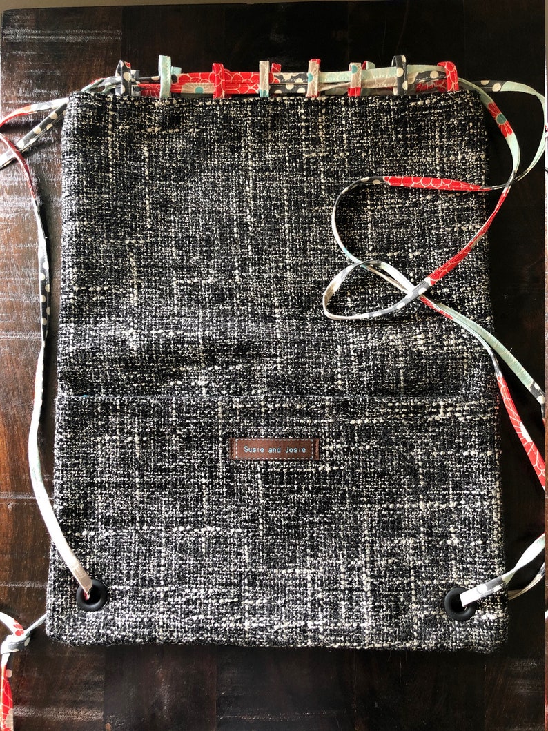 May include: A black and white woven drawstring bag with a brown leather tag that says "Susie and Josie". The bag has a floral patterned fabric trim.