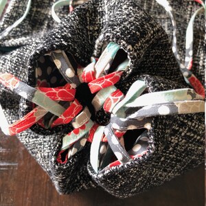 May include: A black and white drawstring bag with a fabric lining featuring red, white, and blue floral patterns. The bag is closed with a drawstring made of the same fabric.
