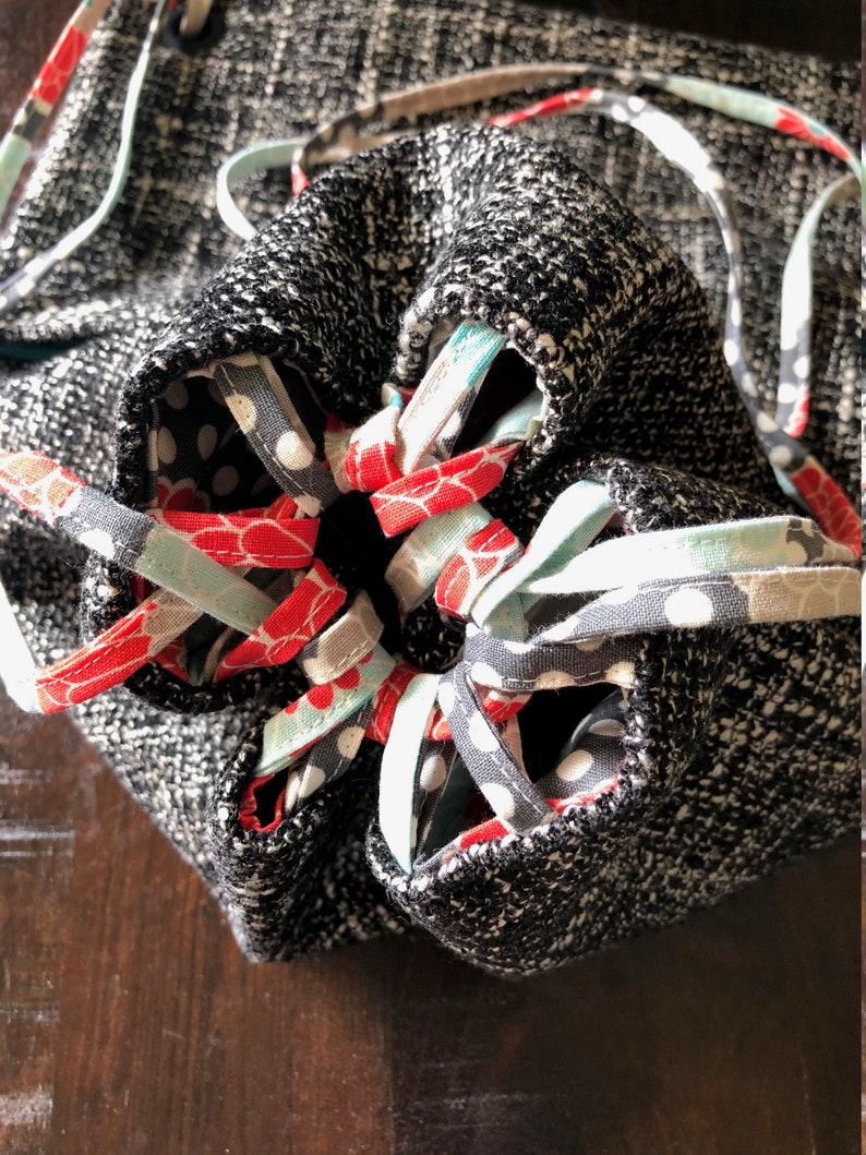 May include: A black and white drawstring bag with a fabric lining featuring red, white, and blue floral patterns. The bag is closed with a drawstring made of the same fabric.