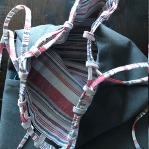 May include: A gray canvas tote bag with red and white striped fabric lining. The bag has a drawstring closure with white and red striped cords.