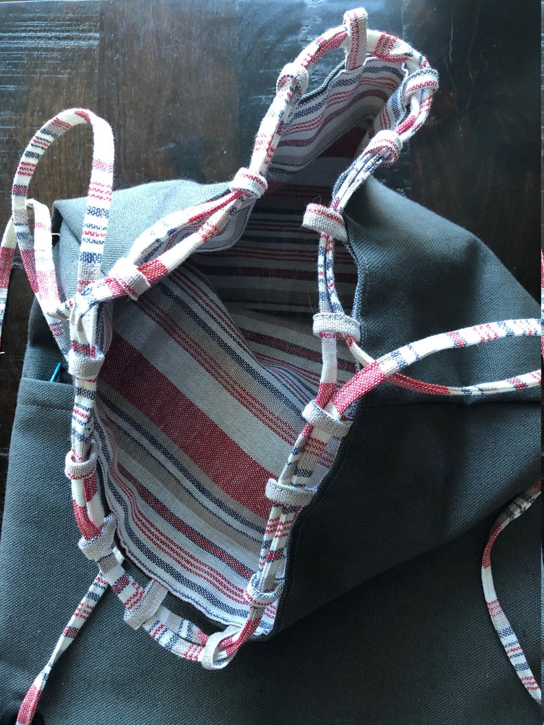 May include: A gray canvas tote bag with red and white striped fabric lining. The bag has a drawstring closure with white and red striped cords.
