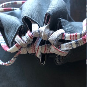 May include: A gray drawstring bag with a white and red striped drawstring. The bag is made of a soft, textured fabric.