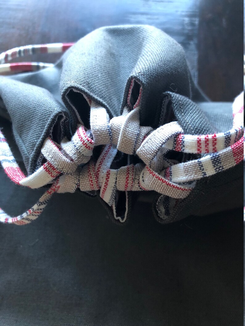 May include: A gray drawstring bag with a white and red striped drawstring. The bag is made of a soft, textured fabric.
