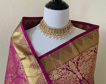 May include: A green and magenta silk saree with gold embroidery and a pearl and gold necklace.