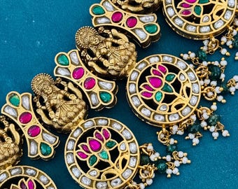 May include: A gold necklace with intricate detailing, featuring a repeating pattern of a goddess figure and a lotus flower. The necklace is adorned with pink and green gemstones, and white pearls.