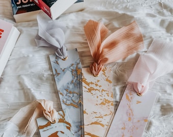 May include: Four marble-patterned bookmarks with gold accents and different colored ribbons. The bookmarks are on a white surface.