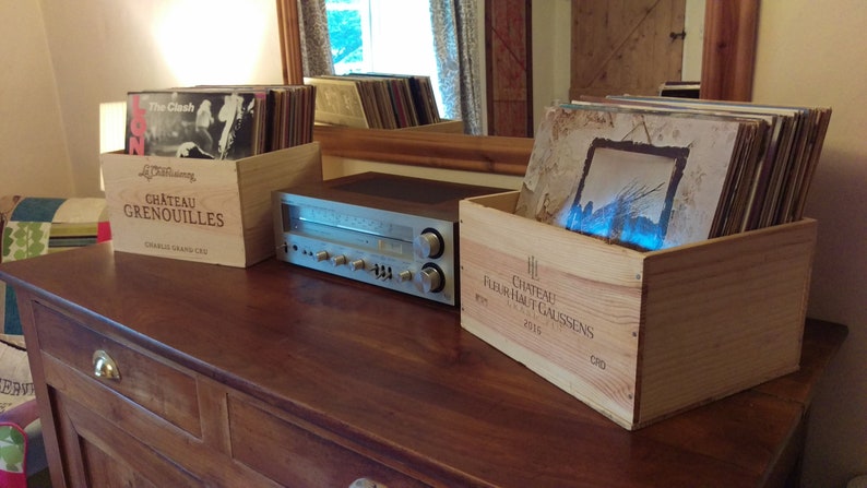 Pu&ograve; includere: Due casse di legno per vino, una etichettata "Chateau Grenouilles" e l'altra "Chateau Haut Caussens", sono utilizzate per riporre dischi in vinile. Un ricevitore stereo argentato si trova su un tavolo di legno tra le casse.