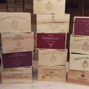 Pu&ograve; includere: Una pila di casse di vino in legno con diverse etichette. Le casse sono impilate a forma di piramide e sono in legno marrone chiaro. Le etichette sono stampate in bianco e nero e presentano i nomi di diversi vini. Alcune etichette sono in francese, mentre altre sono in inglese.