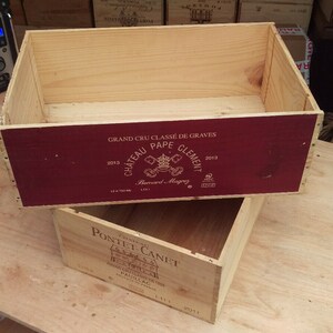 Pu&ograve; includere: Due casse di legno per vino impilate l'una sull'altra. La cassa superiore &egrave; etichettata "GRAND CRU CLASS&Eacute; DE GRAVES 2013 CHATEAU PAPE CLEMENT 2018". La cassa inferiore &egrave; etichettata "PONTET-CANET 2011".