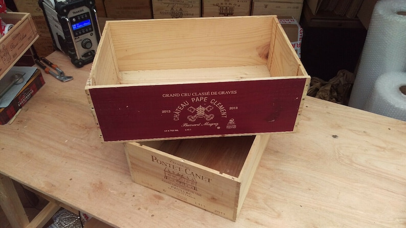 Pu&ograve; includere: Due casse di legno per vino impilate l'una sull'altra. La cassa superiore &egrave; etichettata "GRAND CRU CLASS&Eacute; DE GRAVES 2013 CHATEAU PAPE CLEMENT 2018". La cassa inferiore &egrave; etichettata "PONTET-CANET 2011".