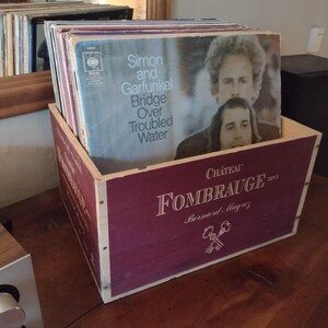 Pu&ograve; includere: Una scatola di legno con un coperchio color borgogna e un bordo bianco. Il coperchio ha stampato il testo "Ch&acirc;teau FOMBRAUGE 2003 Bernard, Magny". La scatola &egrave; piena di dischi in vinile, tra cui uno con la copertina dell'album "Simon and Garfunkel Bridge Over Troubled Water".