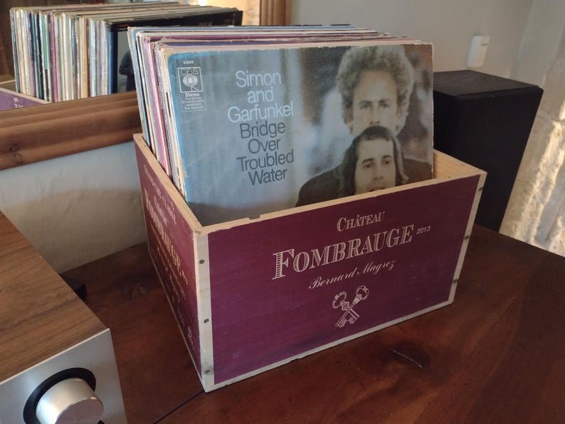 Pu&ograve; includere: Una scatola di legno con un coperchio color borgogna e un bordo bianco. Il coperchio ha stampato il testo "Ch&acirc;teau FOMBRAUGE 2003 Bernard, Magny". La scatola &egrave; piena di dischi in vinile, tra cui uno con la copertina dell'album "Simon and Garfunkel Bridge Over Troubled Water".